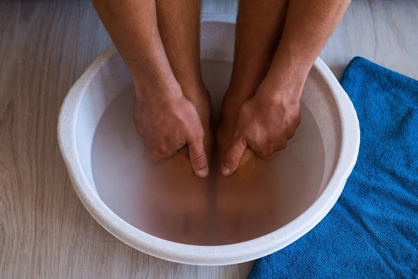 Male put hands and feet in bath with hot water and baking soda at home. Homemade bath soak for dry feet skin