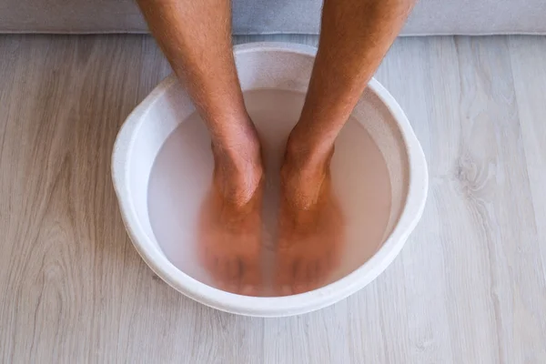 Man membuat mandi dengan air panas dan baking soda untuk kakinya. Mandi buatan sendiri rendam untuk kulit kaki kering — Stok Foto
