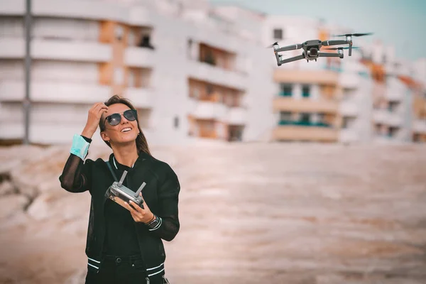 Cute nowoczesny uśmiechnięta pani pilot w ciemnych stylowych ubrań kontroluje drona z pilotem. hobby na świeżym powietrzu. — Zdjęcie stockowe