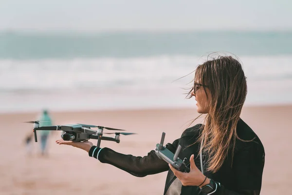 Cute modern lady pilot lands drone on her hand with remote controller. Outdoors hobby.