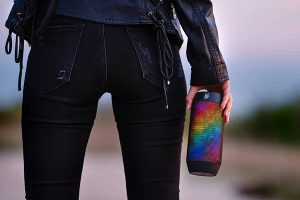 Sexy vrouw in zwarte kleding met LED portable JBL multicolour draadloze bluetooth luidsprekers. Luisteren en genieten van de muziek buiten. — Stockfoto