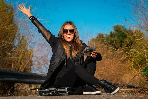 Jonge moderne vrouw in stijlvolle donkere kleding en zonnebril is erg blij om te beginnen vliegen drone in de zonnige herfstdag. Buitenhobby — Stockfoto