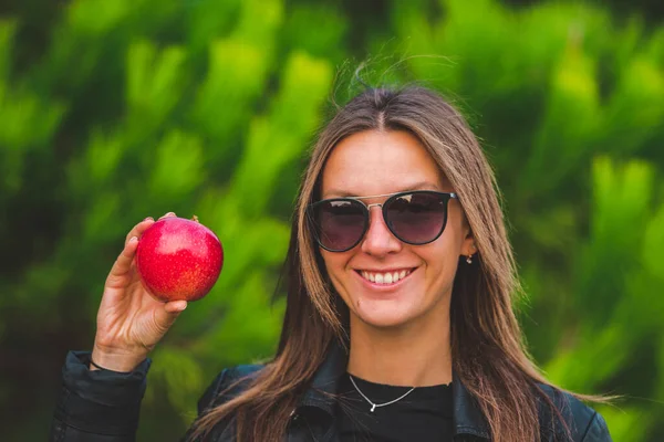 Smiling vegan woman showing red tasty apple on a green background. Healthy lifestyle concept. Natural vitamins