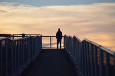 Uzaktaki yaya köprüsünde yalnız bir adamın silueti. 