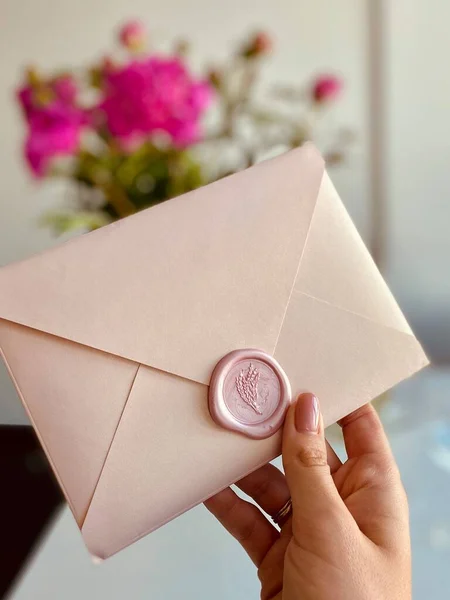 Letter in a pink envelope or invitation in the hand girl's on the background pink flowers peonies