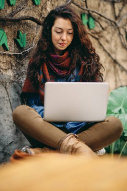 Dizüstü bilgisayar kullanarak ve bahçede otururken gülümseyen kadın.