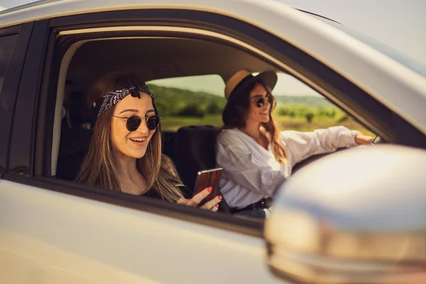 两个女孩在车里开车 一个驾驶和其他使用智能手机短信 — 图库照片
