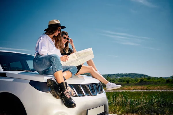 Girls sitting on the car and reading map.