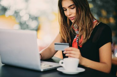 Seçici odak kafede otururken alışveriş için kredi sepeti ve dizüstü bilgisayar kullanan kadın.