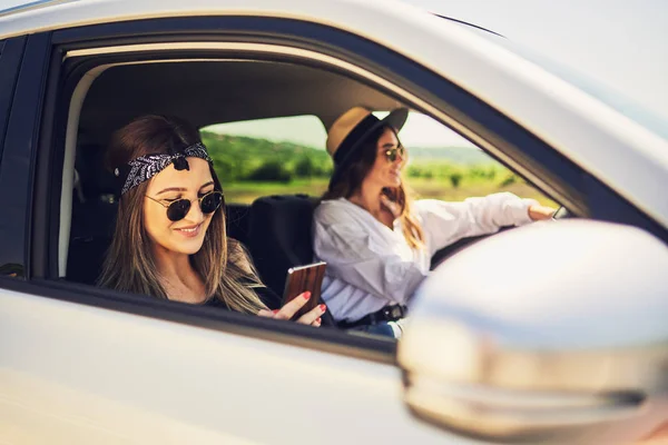 两个女孩在车里开车 一个女孩驾驶和其他使用智能手机短信 — 图库照片