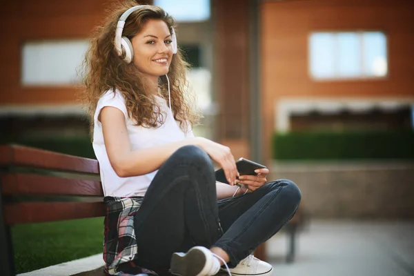 Mujer Joven Sentada Banco Con Las Piernas Cruzadas Escuchando Música — Foto de Stock