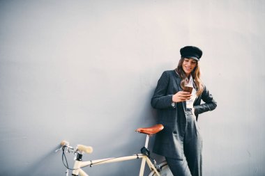 Duvara karşı duran ve akıllı telefon mesaj attığın için kullanarak kadın. Yanındaki sarı Onun Bisiklet.