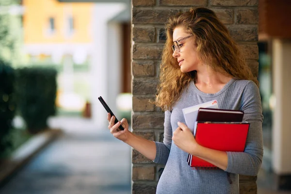 Profesora Sosteniendo Libros Usando Teléfono Inteligente Mientras Apoya Pilar Ladrillo — Foto de Stock