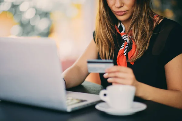 Happy young woman using credit card and laptop for shopping while sitting in cafe.