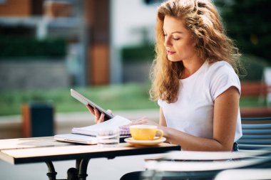 Tablet kullanma ve kafede kahve içme kız öğrenci. Kitap ve defter bir tablo üzerinde.