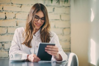 Kafede oturan ve tablet kullanarak genç modern kadın.