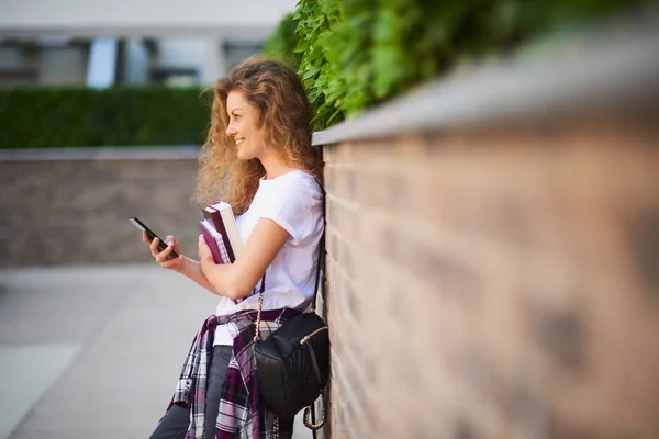 女学生在校园漫步时使用智能手机和手持书本 — 图库照片