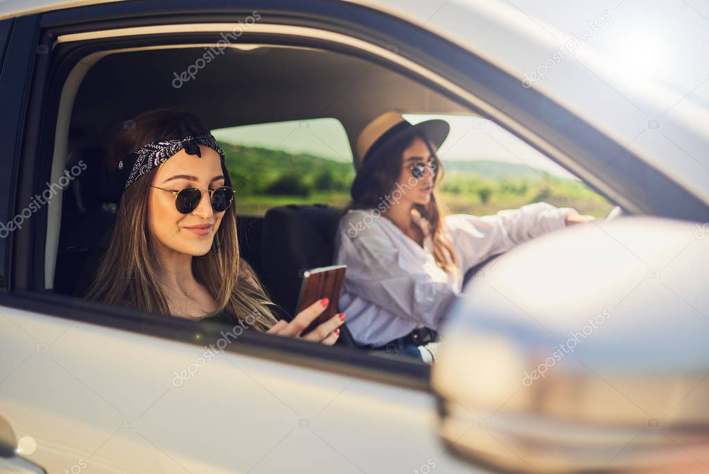Two girls driving in the car. One girl driving and other using s