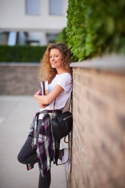 Kollarındaki ve çanta kitaplarda omuz ile duvara karşı duran kız öğrenci.