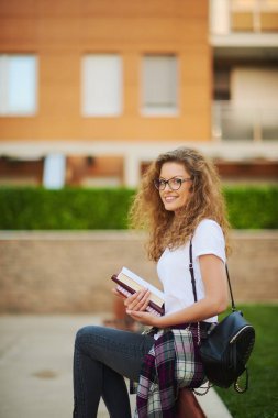 Başlamak için bir kampüs içinde oturan ve sınıf için bekleyen kız öğrenci. El kitaplarında.