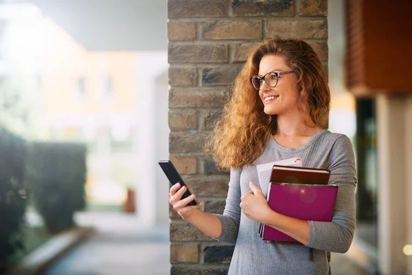 Female Professor Holding Books Using Smart Phone While Leaning Brick — Stock Photo, Image