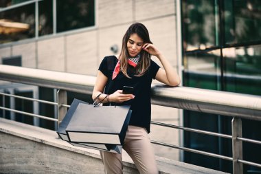 Alışveriş torbaları tutarak ve alışveriş merkezi önünde akıllı telefon kullanan kadın.