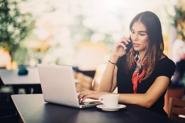 Kafede otururken eğlenceliydi telefon ve dizüstü bilgisayar kullanan kadın portresi.