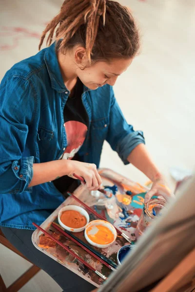 Sanatsal kız stüdyoda oturan ve resim için renkleri karıştırma.