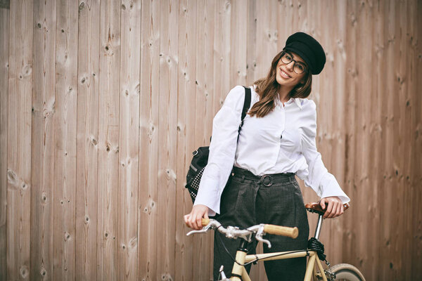 Portrait of beautiful brunette holding bicycle. Wooden background.