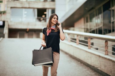 Alışveriş torbaları tutarak ve alışveriş merkezi önünde akıllı telefon kullanan kadın.