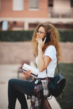 Kadın srudent akıllı telefonda konuşurken ve Kitaplar bankta otururken holding.