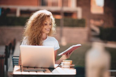 Kız öğrenci kompozisyon için kafede otururken dizüstü bilgisayar kullanarak.