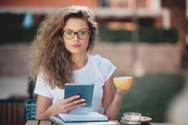 Tablet kullanma ve kafede kahve içme kız öğrenci. Kitap ve defter bir tablo üzerinde.