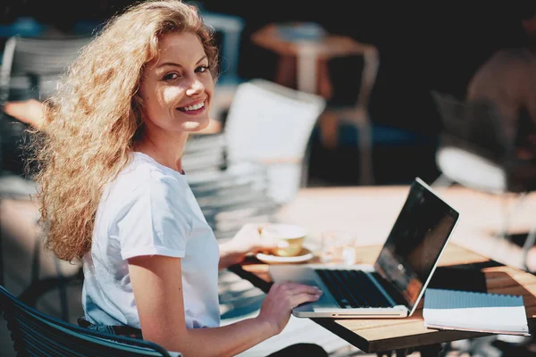 Female student drinking coffee and using laptop while sitting in cafe.