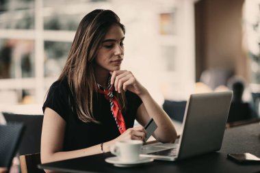 Kafede otururken alışveriş için kredi kartı ve dizüstü bilgisayar kullanan mutlu genç kadın.