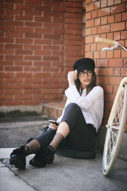 Kaldırımda oturan ve akıllı telefon kullanarak kadın. Yanındaki sarı Onun Bisiklet.