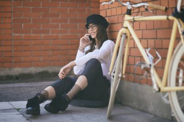 Kaldırımda oturan ve akıllı telefon kullanarak kadın. Yanındaki sarı Onun Bisiklet.