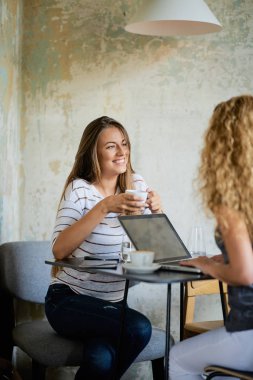 Kafede oturan ve kahve yudumlarken chat yapan iki kadın. Tablo kahve Kupası, dizüstü ve tablet.
