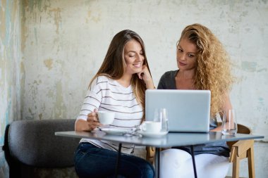 Kafede oturan ve hatta alışveriş için dizüstü bilgisayar kullanarak iki kadın. Su ve kahve kupaları tablo bardak.