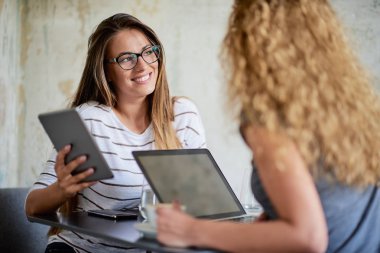 Teknolojileri kullanarak ve içme kahve kafede otururken iki kadın.