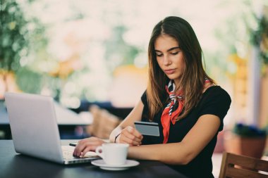 Kafede otururken alışveriş için kredi kartı ve dizüstü bilgisayar kullanan mutlu genç kadın.