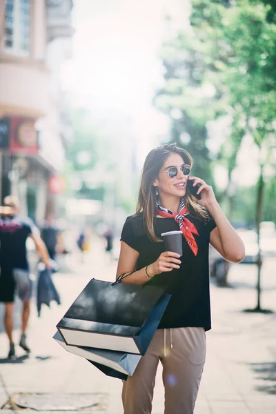 スマート フォンを使用している間ショッピング後路上で紙袋とコーヒーを保持している女性の肖像画 — ストック写真
