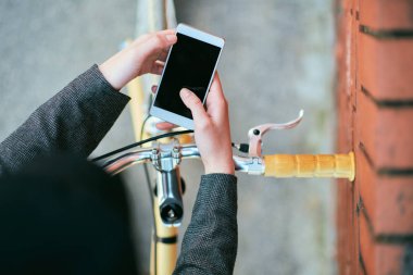 Kız bisiklet üzerinde oturan ve akıllı telefon kullanarak. Akıllı telefon üzerinde seçici odak.