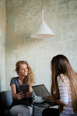 Teknolojileri kullanarak ve içme kahve kafede otururken iki kadın.