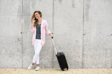 Akıllı telefon ve holding Bagaj duvara karşı dururken kullanan kadın.