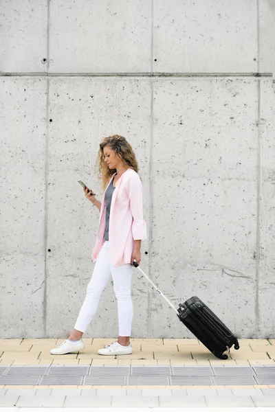 妇女携带行李和使用智能手机 而步行到车站 — 图库照片