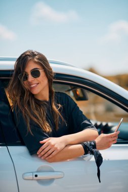 Araba camına eğilerek akıllı telefon kullanan kadın.