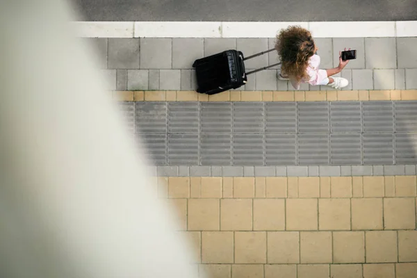 Top view of woman holding smart phone and luggage while going to the station/airport.