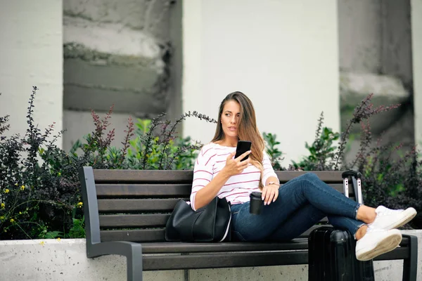 Mujer Sentada Banco Usando Teléfono Inteligente Mientras Espera Estación Piernas —  Fotos de Stock