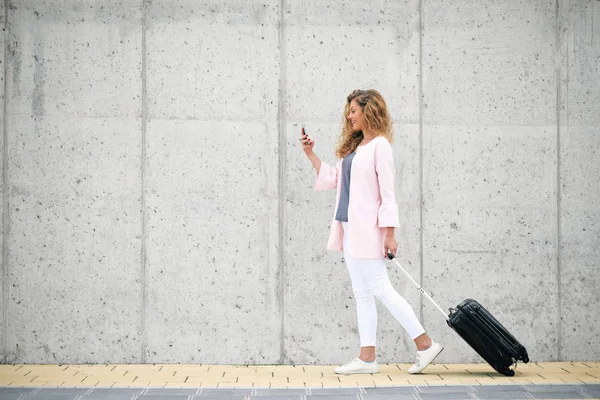 妇女携带行李和使用智能手机 而步行到车站 — 图库照片